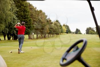Mature Male Golfer Hitting Tee Shot Along Fairway With Driver Viewed Through Buggy Window