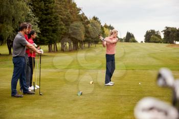 Two Couples Golfing Hitting Tee Shot Along Fairway With Driver With Clubs In Foreground