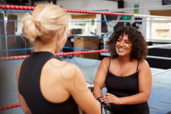 Personal Trainer Helping Female Boxer In Gym To Put On Boxing Gloves In Gym