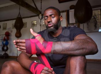 Male Boxer Training In Gym Wraps On Hands Standing Next To Punching Bag