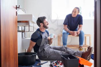Male Plumber With Female Apprentice Taking A Break From Fixing Leaking Sink In Home Bathroom