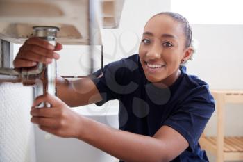 Portrait Of Female Plumber Working To Fix Leaking Sink In Home Bathroom