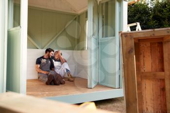 Couple Taking A Break From Building Outdoor Summerhouse In Garden
