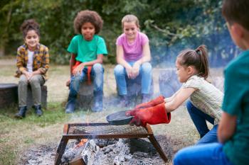 Group Of Children On Outdoor Activity Camping Trip Cooking Over Camp Fire Together