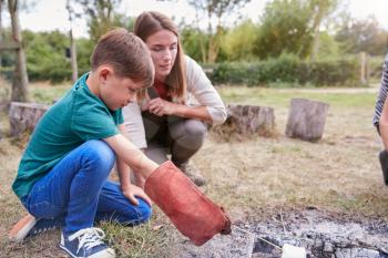 Female Team Leader With Boy On Outdoor Activity Trip Toasting Marshmallows Over Camp Fire