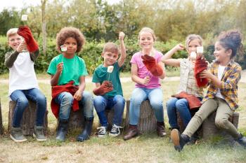 Portrait Of Children On Outdoor Activity Camping Trip Eating Marshmallows Around Camp Fire Together