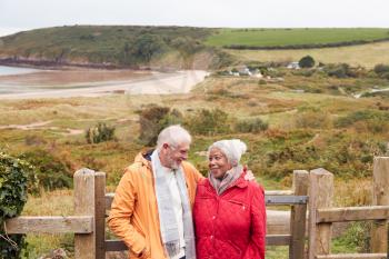 Loving Active Senior Couple Resting By Gate As They Walk Along Coastal Path In Winter