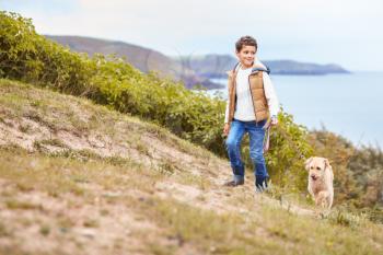 Boy Exercising Dog On Leash Walking Up Hill By Sea