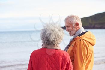 Rear View Of Senior Couple Holding Hands Looking Out To Sea On Winter Beach Vacation