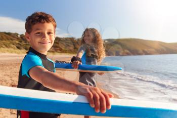 Portrait Of Children Wearing Wetsuits Carrying Bodyboards On Summer Beach Vacation Having Fun By Sea