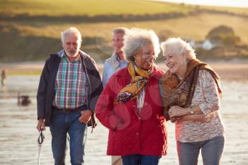 Group Of Smiling Senior Friends Walking Arm In Arm Along Shoreline Of Winter Beach