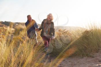 Loving Active Senior Couple Holding Hands As They Walk Through Sand Dunes