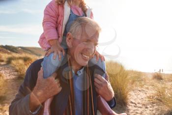 Grandfather Giving Granddaughter Ride On Shoulders As They Walk Through Sand Dunes