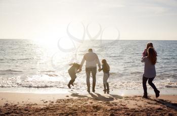 Rear View Of Family Jumping Over Waves Looking Out To Sea Silhouetted Against Sun