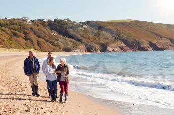 Senior Couple Walking Along Shoreline With Adult Offspring On Winter Beach Vacation