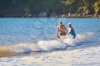 Loving Senior Couple Holding Hands As They Walk Into Sea For Swim