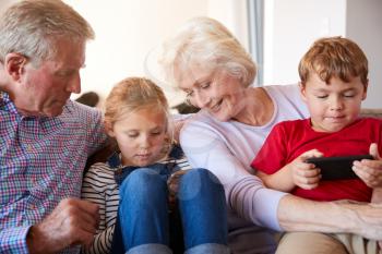 Grandparents Playing Video Games With Grandchildren On Mobile Phones At Home