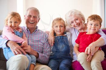Portrait Of Grandparents Sitting On Sofa At Home With Grandchildren