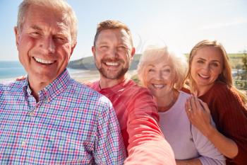 Portrait Of Senior Couple With Adult Offspring Posing For Selfie On Vacation By The Sea