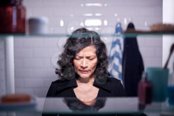 View Through Bathroom Cabinet Of Unhappy Mature Businesswoman Getting Ready For Work