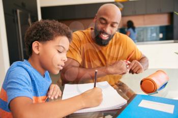 African American Father Helping Son Studying Homework In Kitchen