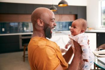 Smiling Stay At Home African American Father Cuddling And Playing With Baby Daughter Indoors At Home