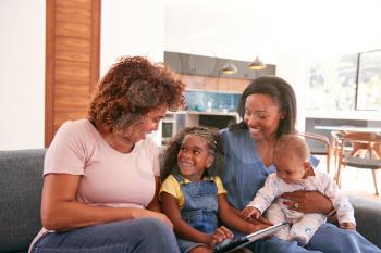 Multi-Generation Female African American Family Sitting On Sofa At Home Using Digital Tablet