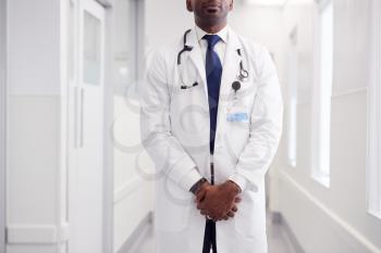 Close Up Of Mature Male Doctor Wearing White Coat Standing In Hospital Corridor