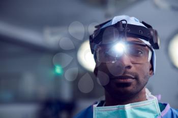 Portrait Of Male Surgeon Wearing Protective Glasses And Head Light In Hospital Operating Theater
