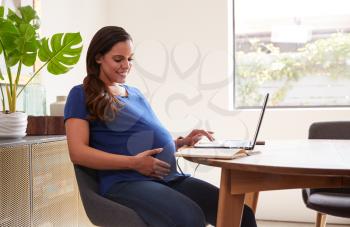 Pregnant Woman Using Laptop At Table Working From Home