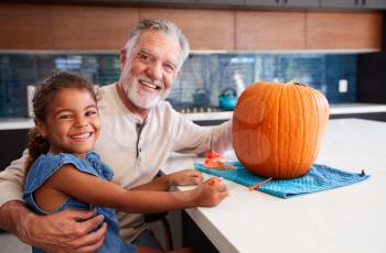 Portrait Of Grandfather And Granddaughter Carving Halloween Lantern From Pumpkin At Home