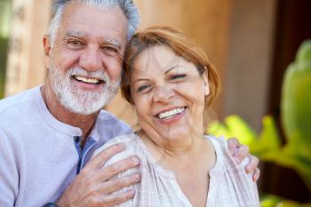 Portrait Of Smiling Senior Hispanic Couple Relaxing In Garden At Home Together