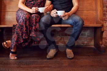 Close Up On Feet Of Couple Sitting On Bench In Coffee Shop Together