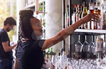 Female Bartender Arranging Bottles Of Alcohol Behind Bar