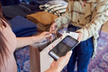 Woman In Clothing Store Making Contactless Payment With App On Mobile Phone