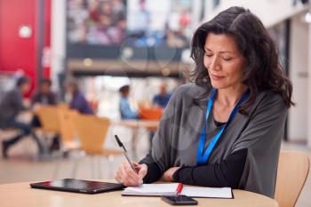 Mature Female Teacher Or Student With Digital Tablet Working At Table In College Hall