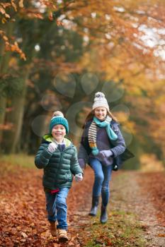 Portrait Of Two Smiling Children Having Fun Running Along Path Through Autumn Woodland Together