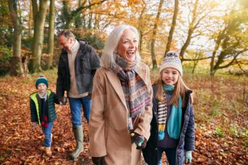 Grandparents With Grandchildren Enjoying Walk Along Autumn Woodland Path Together