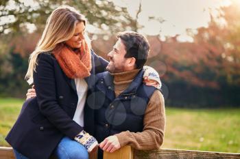 Loving Couple On Walk Through Autumn Countryside Sitting On Gate