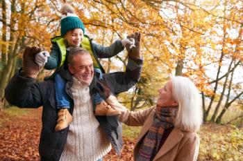 Grandparents With Grandson Enjoying Walk Along Autumn Woodland Path Together