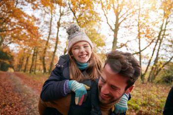 Father Giving Laughing Daughter Piggyback Ride On Family Walk Through Autumn Woodland