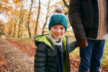 Portrait Of Son Holding Fathers Hand On Family Walk Through Autumn Woodland Landscape
