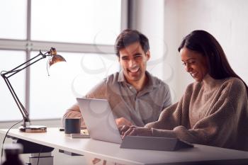 Businesswoman Working On Laptop At Desk Collaborating With Male Colleague