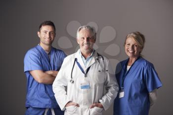 Studio Portrait Of Three Members Of Medical Team Wearing Scrubs Standing Against Grey Background