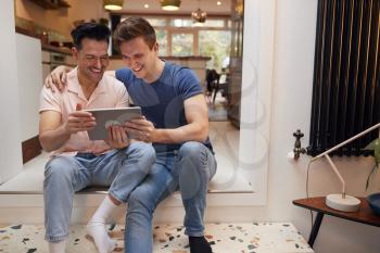 Loving Same Sex Male Couple Using Digital Tablet As They Relax At Home Together