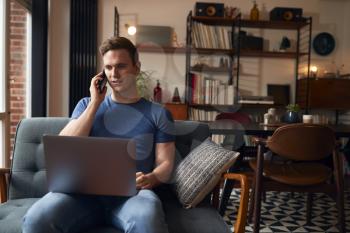 Man Working From Home On Laptop Making Call On Mobile Phone