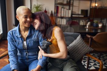 Loving Same Sex Female Couple Sitting On Sofa At Home Gaming Together