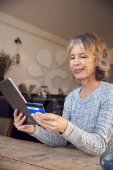 Mature Woman At Home Buying Products Or Services Online Using Digital Tablet And Credit Card