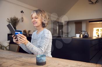 Mature Woman At Home Buying Products Or Services Online Using Digital Tablet And Credit Card