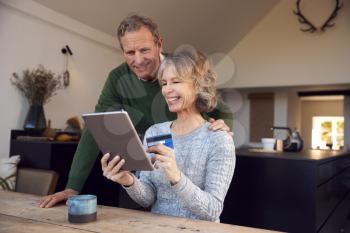 Retired Senior Couple At Home Buying Products Or Services Online With Digital Tablet And Credit Card